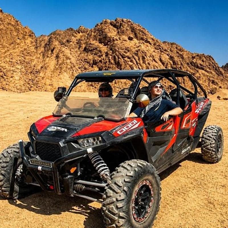 Family buggy safari: two guests in a red four-seat off-road buggy below rocky desert mountains