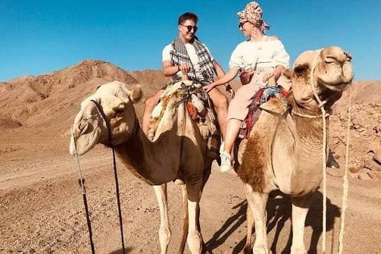 Couple riding camels side by side in a rocky desert valley