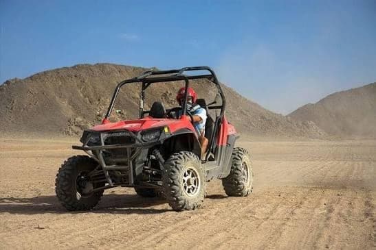 Red two-seat buggy driving through the desert below rocky hills