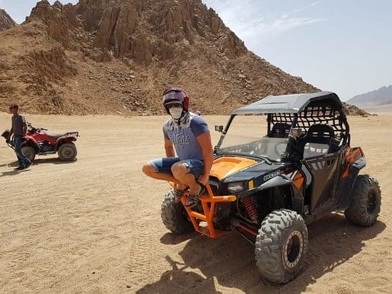 Rider in a helmet sitting on an orange two-seat buggy in a desert valley