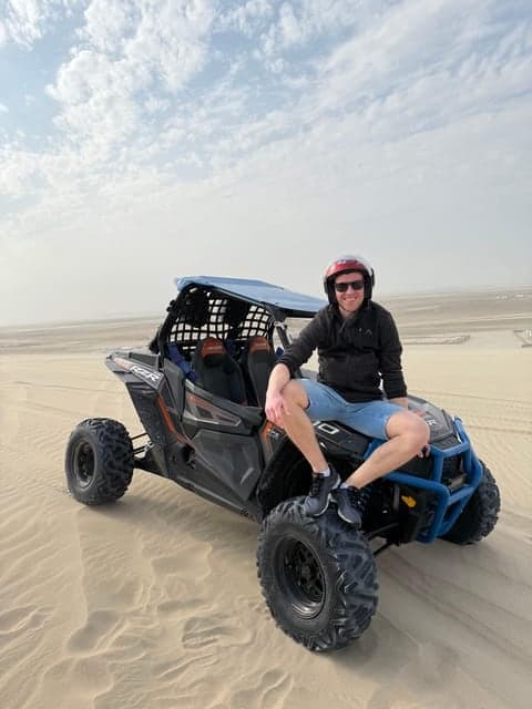 Rider sitting on a buggy on pale sand dunes under a cloudy sky