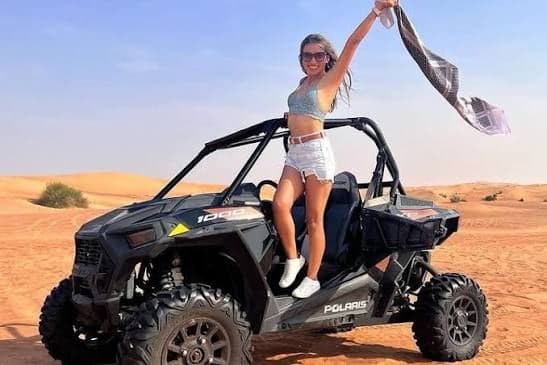 Rider standing on a black buggy and waving a scarf on red sand dunes