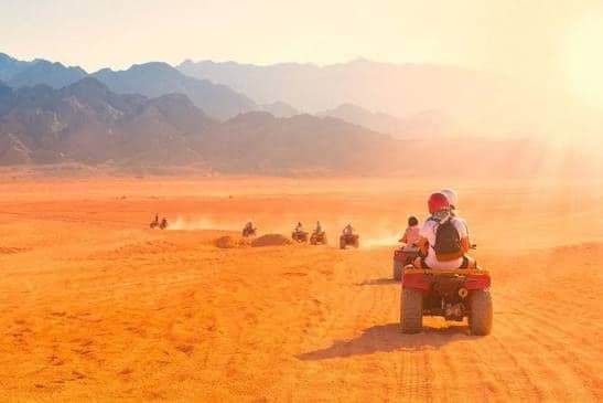 Line of quad bikes crossing orange sand towards the mountains on a Marsa Alam desert safari
