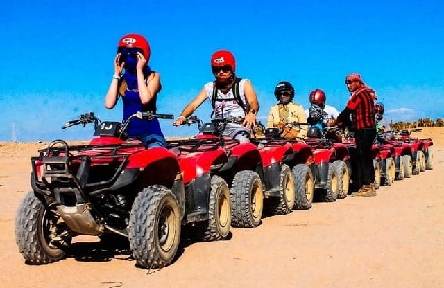 Riders in helmets lined up on red quad bikes before setting off into the desert