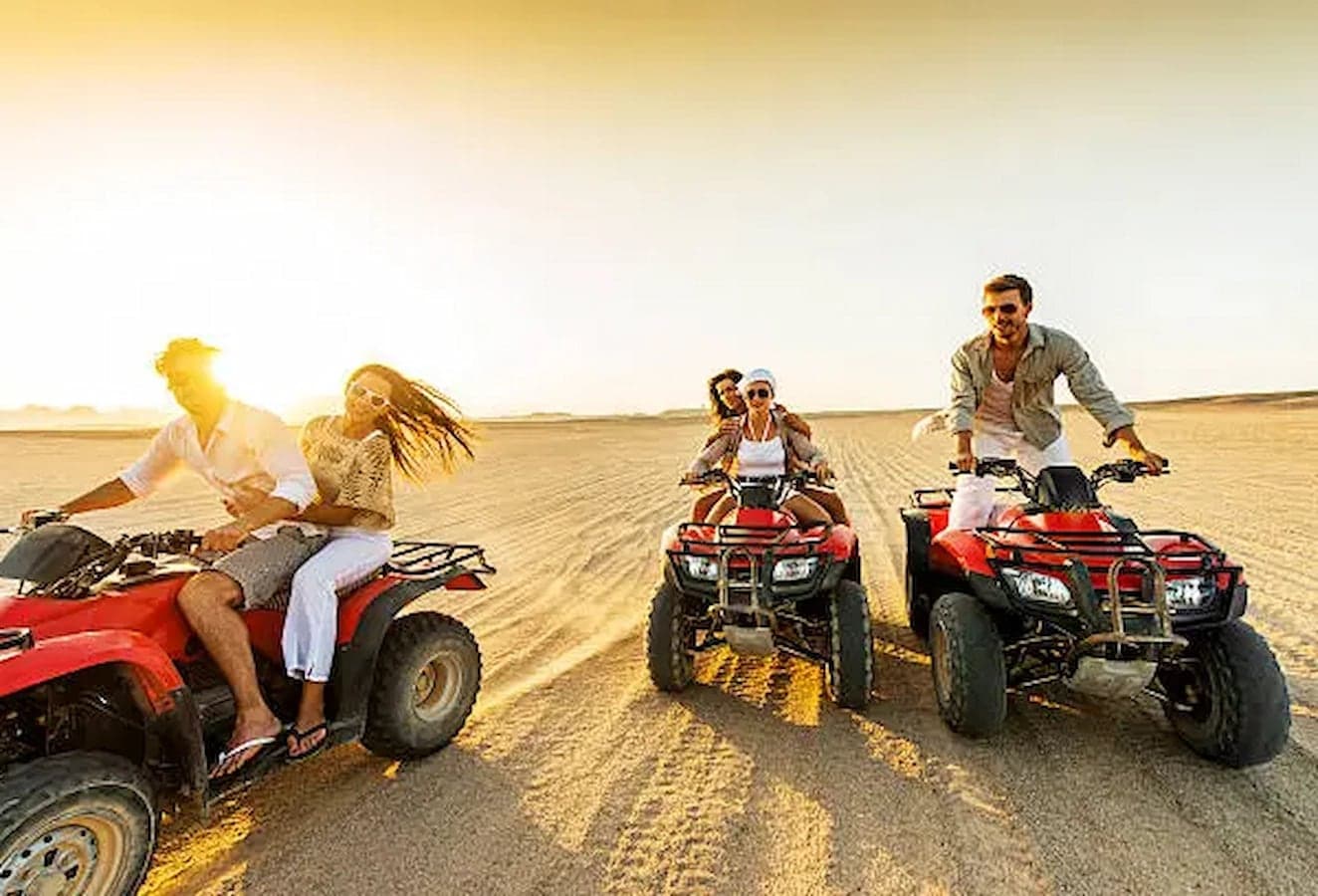 Guests riding quad bikes across the desert in golden evening light on a Marsa Alam desert safari